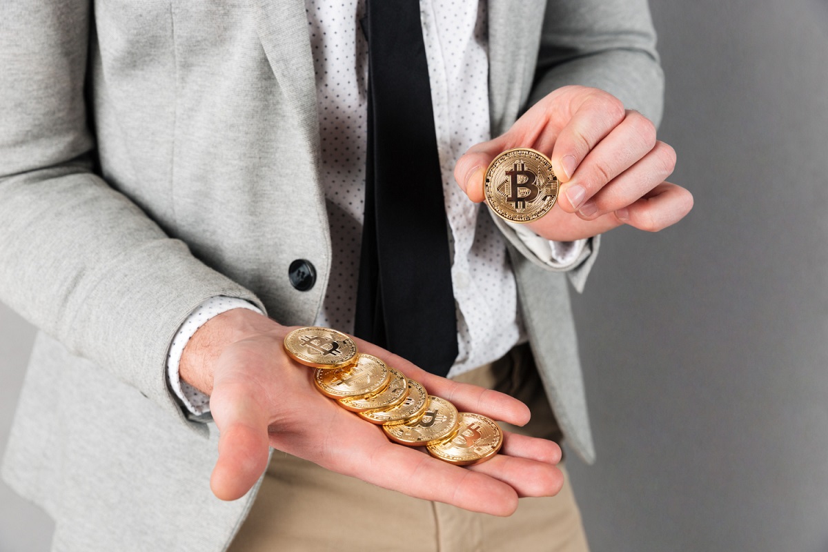 Mão segurando pilha de Bitcoins e outra segurando um Bitcoin