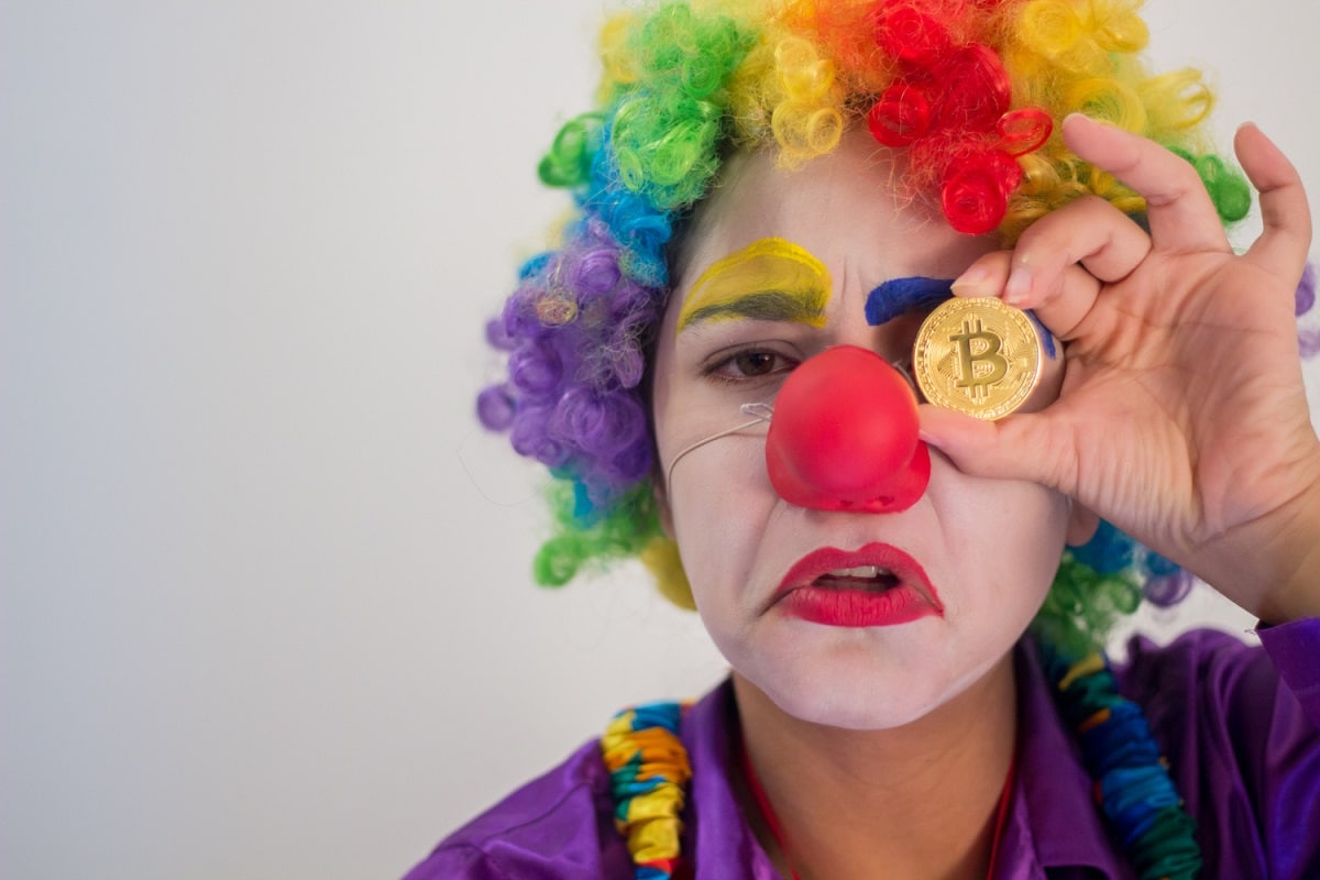 Palhaço segurando moeda Bitcoin perda engano fraude scam golpe criptomoedas altcoins