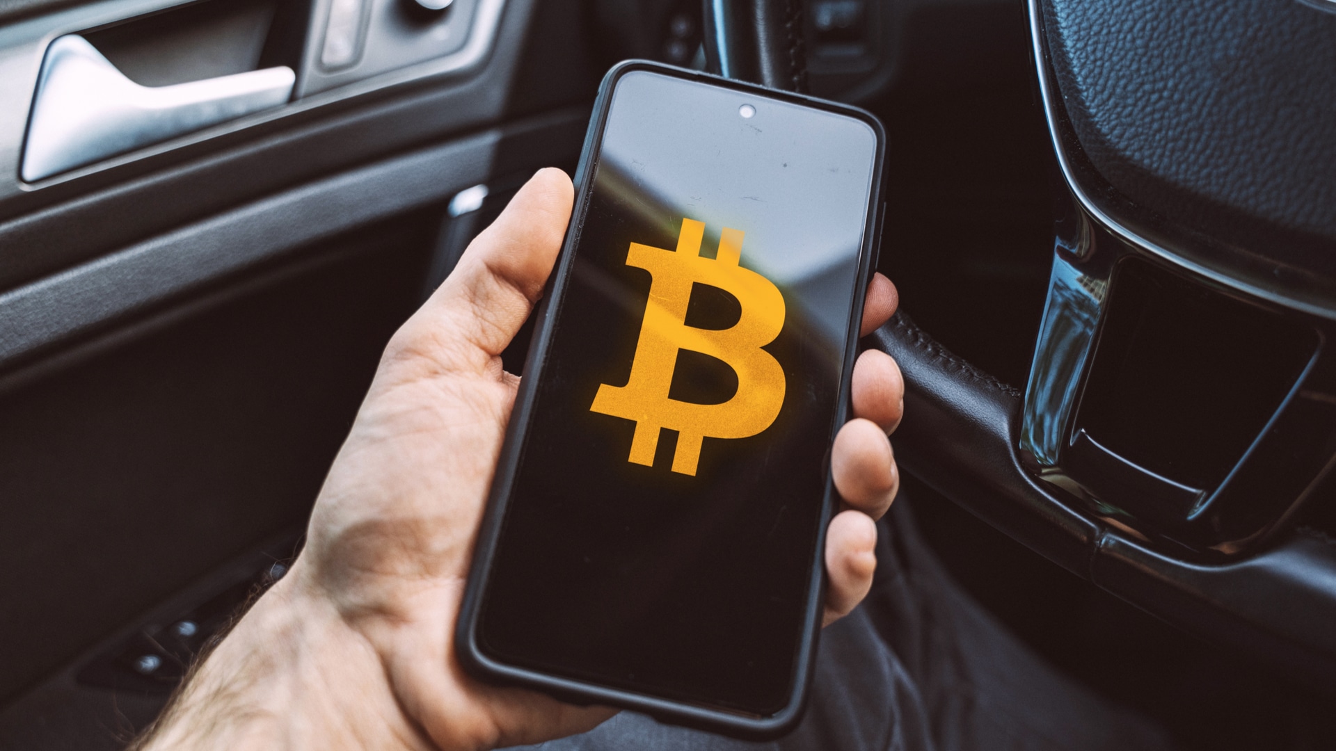Aplicativo de Bitcoin é segurado por pessoa sentada em um carro estacionamento
