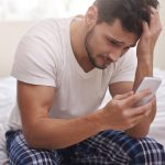 Homem mexendo em celular e sentado na cama estudante perdendo