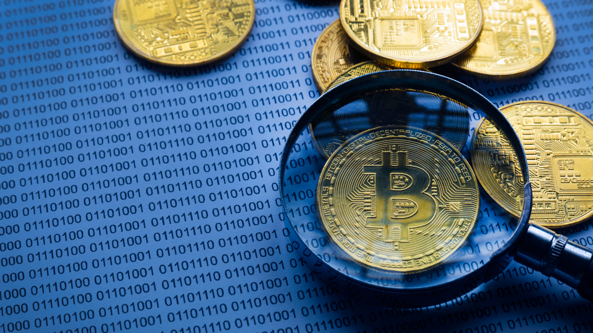 Lupa mostrando Bitcoin em cima de papel com código binário rastreio rastrear procurar vasculhar