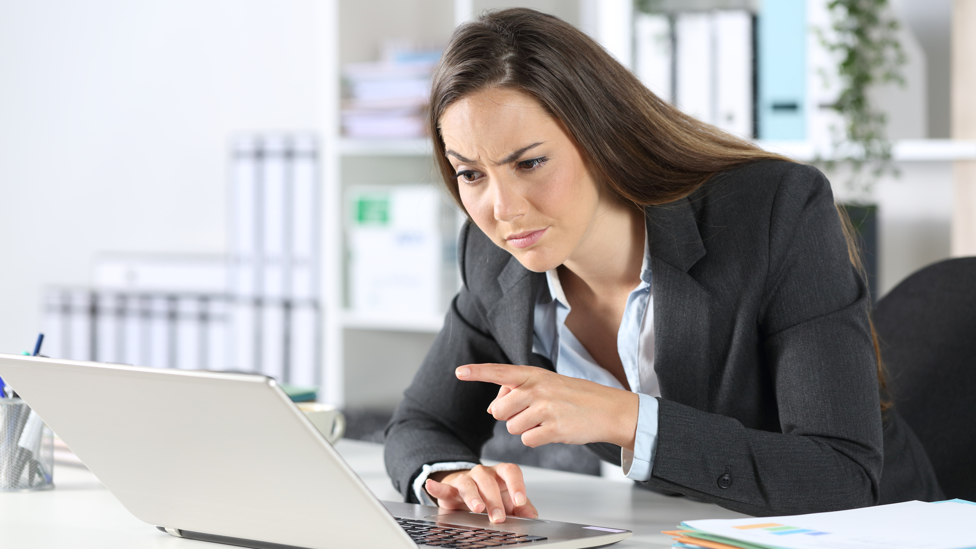 Mulher olhando para notebook e apontando dedo desconfiada