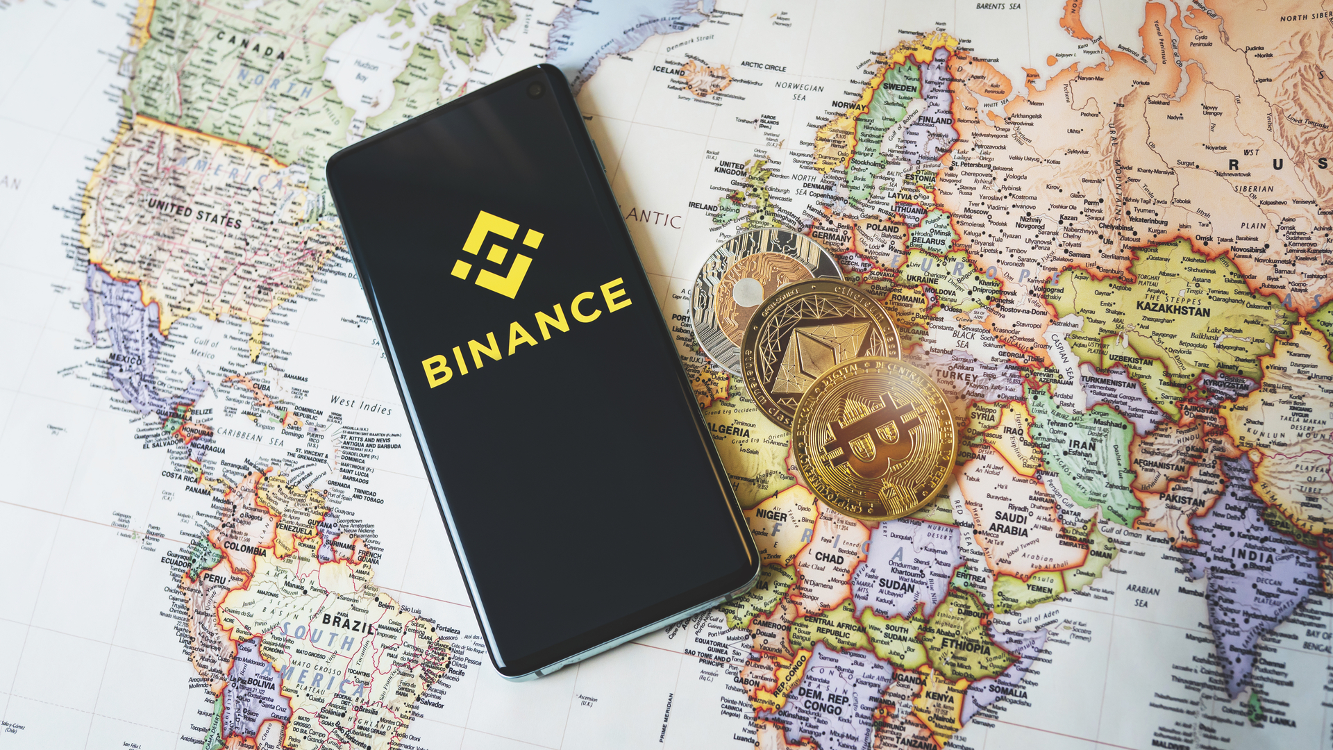 Aplicativo da Binance e criptomoedas em cima de mapa mundial