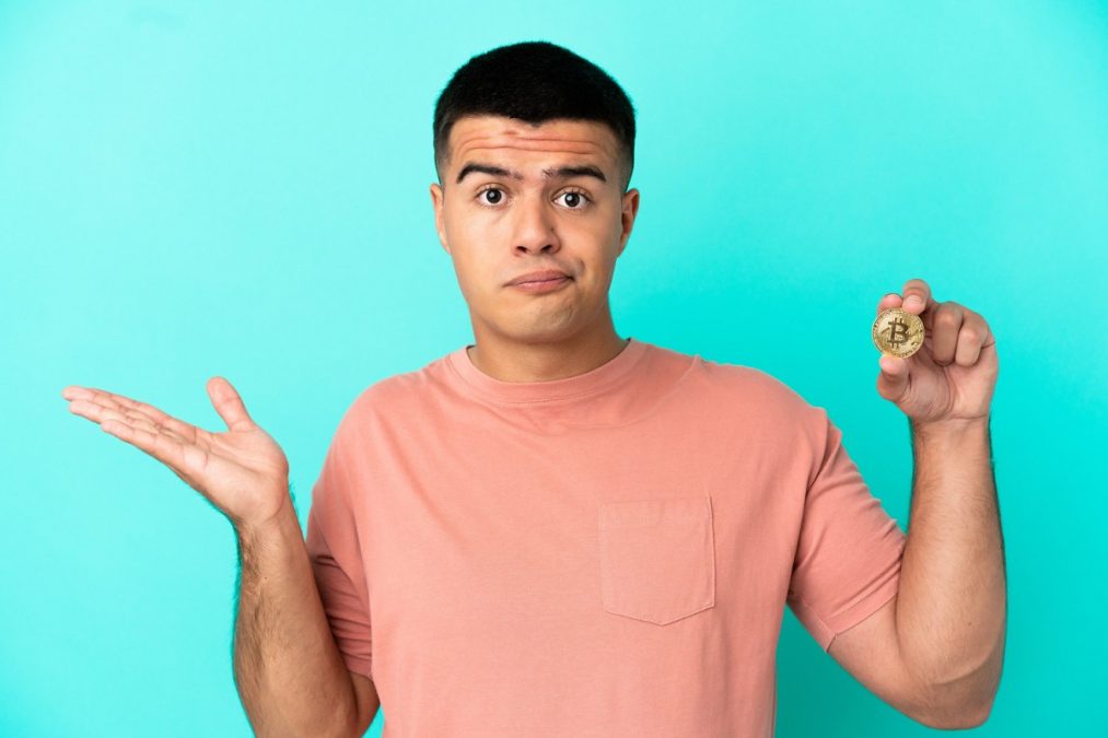 Jovem segurando Bitcoin e em dúvida