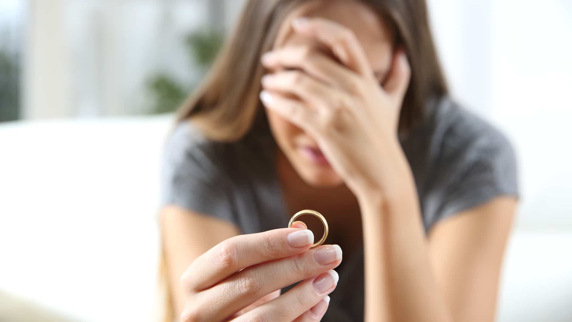 Esposa triste lamentando segurando o anel de casamento