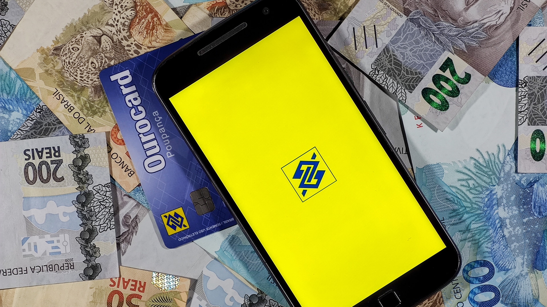 Imagem do aplicativo do Banco do Brasil, com cartão de crédito e dinheiro ao fundo