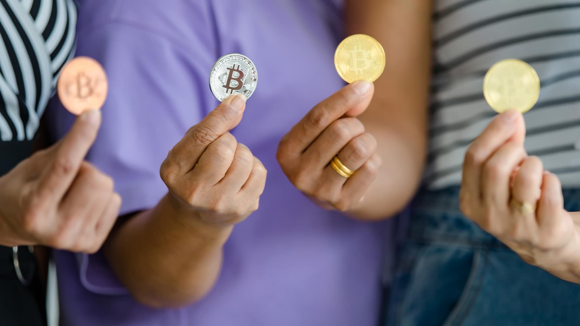 Quatro pessoas segurando moedas físicas de Bitcoin.