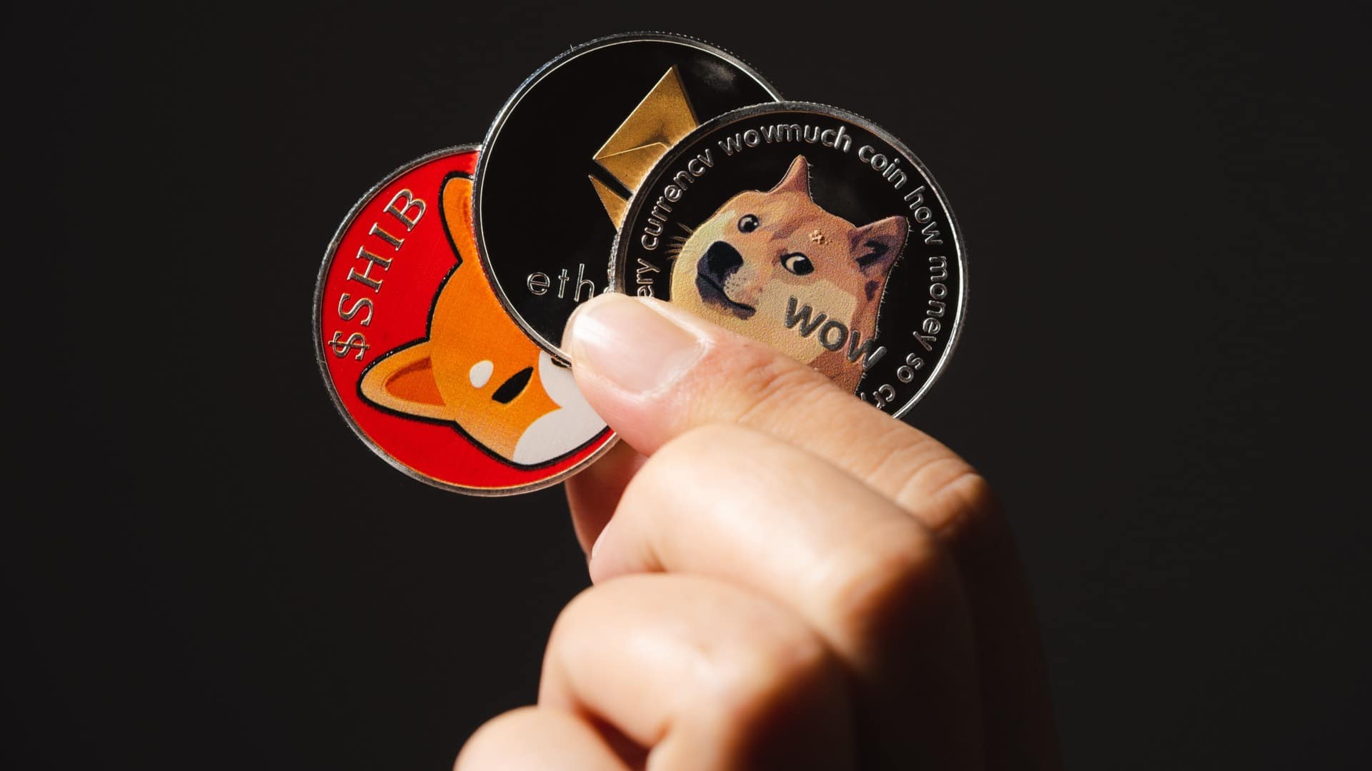 Mão segurando Shiba Inu, Ethereum e Dogecoin