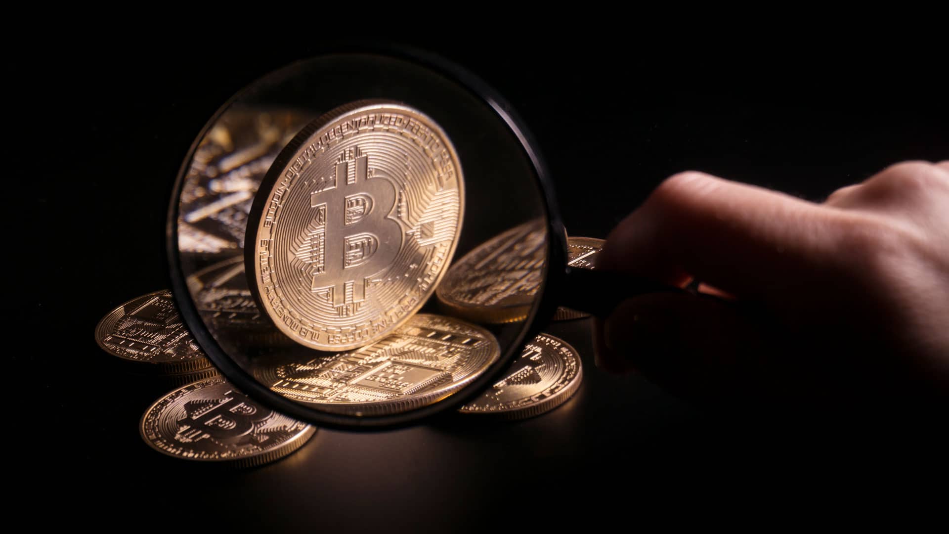 Lupa analisando moeda física de Bitcoin.