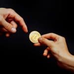Moeda física de Bitcoin sendo passada para outra pessoa.
