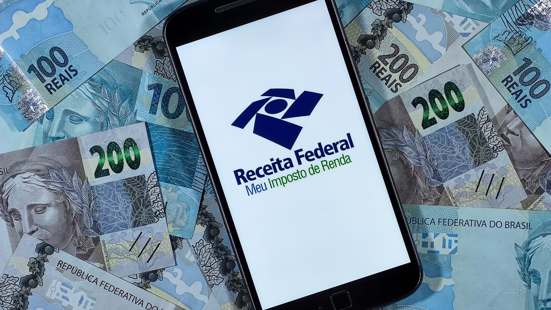 Aplicativo de imposto de renda da Receita Federal cercado de notas de Real
