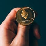 Mão segurando moeda de Ethereum.