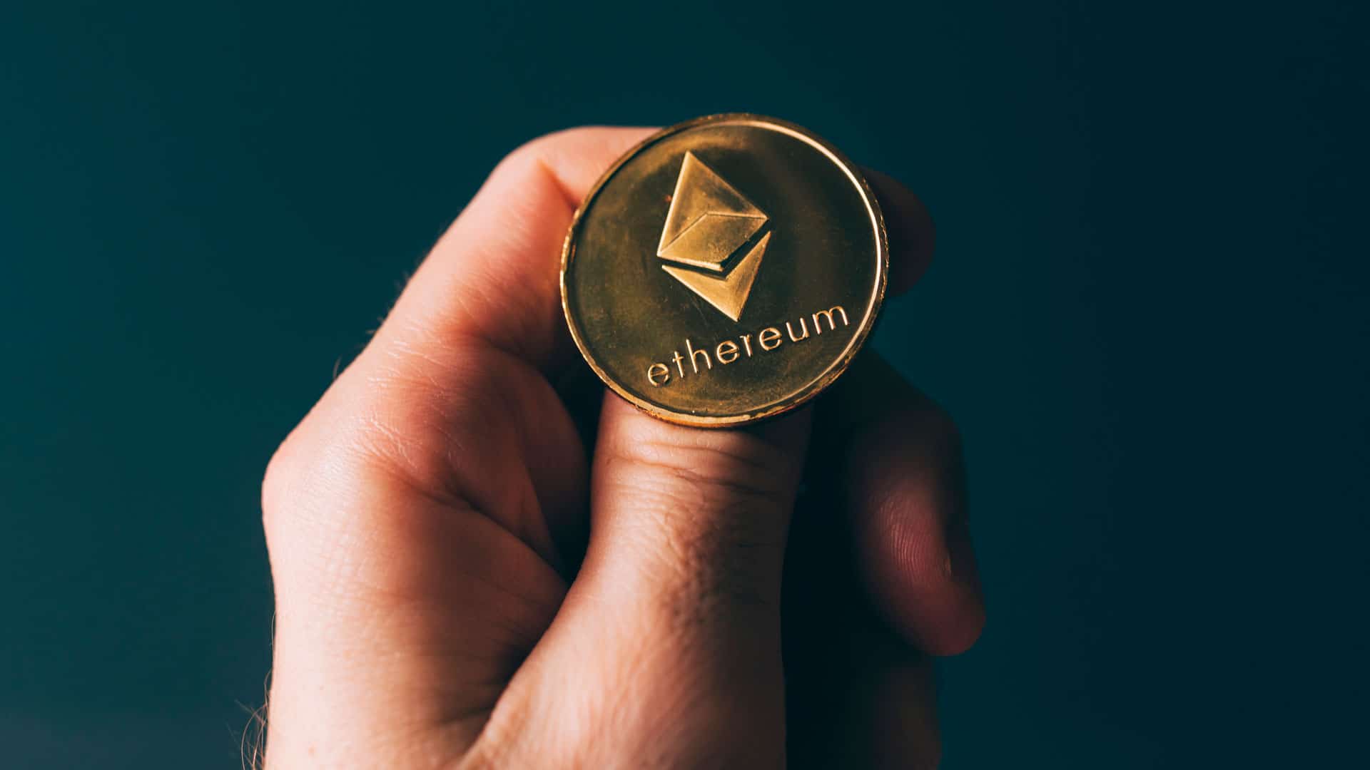 Mão segurando moeda de Ethereum.