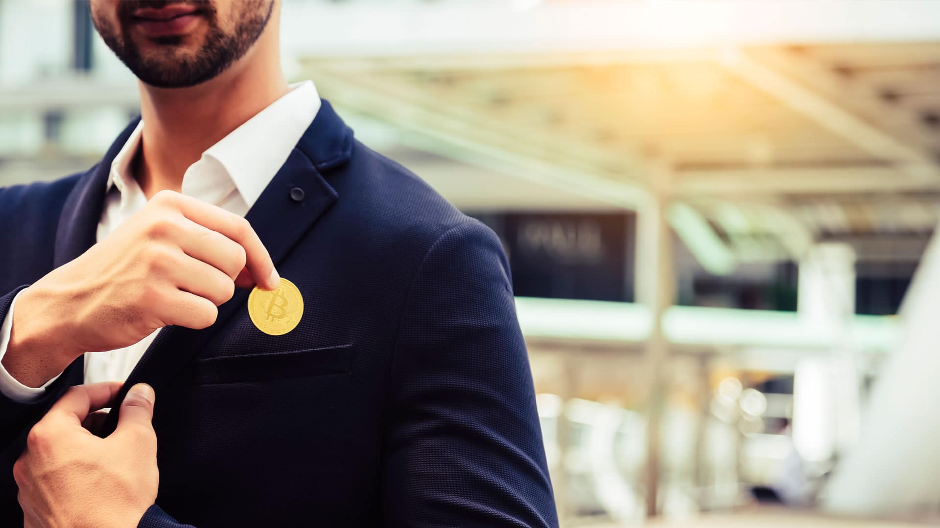 Investidor colocando moeda física de Bitcoin no bolso do terno.