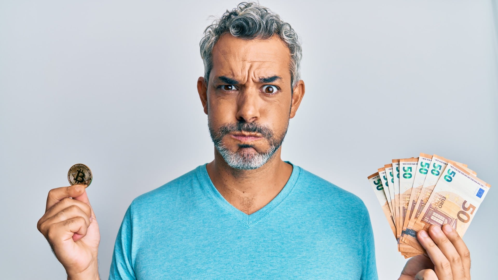 Homem segura notas e Bitcoin preocupado