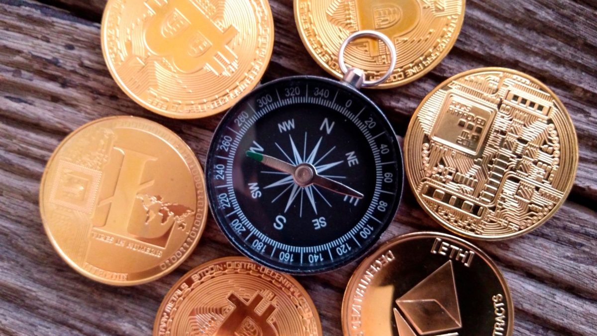 Bússola cercada por moedas físicas de Bitcoin e outras criptomoedas.