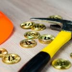 Picareta e moedas físicas de Bitcoin.