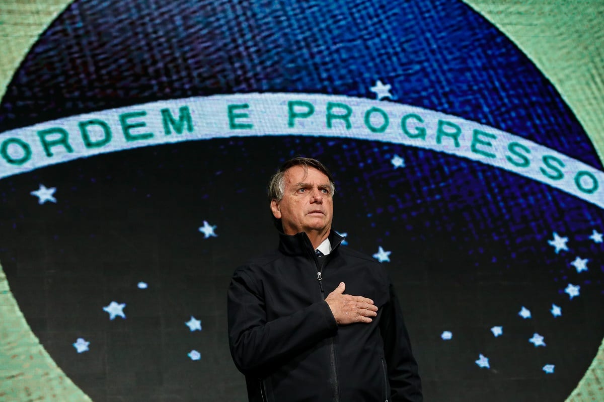 Presidente Jair Bolsonaro com bandeira do Brasil ao fundo