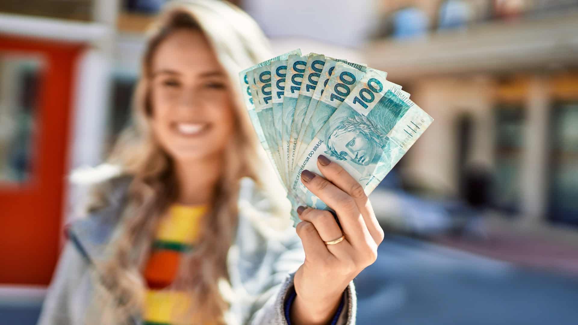 Mulher ao fundo segurando notas de Real brasileiro digital