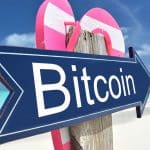 Placa com escrita de Bitcoin apontando para praia