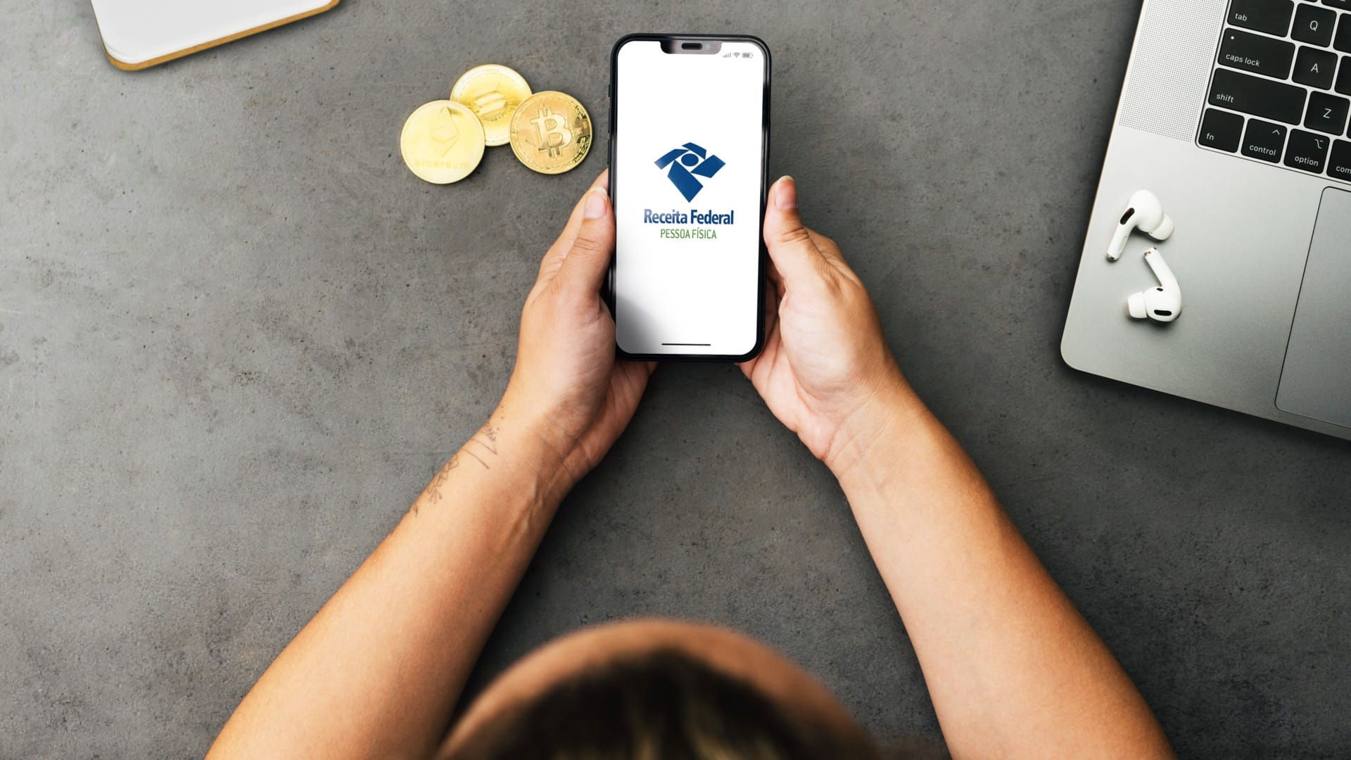 Mulher segurando aplicativo da Receita Federal próximo de criptomoedas