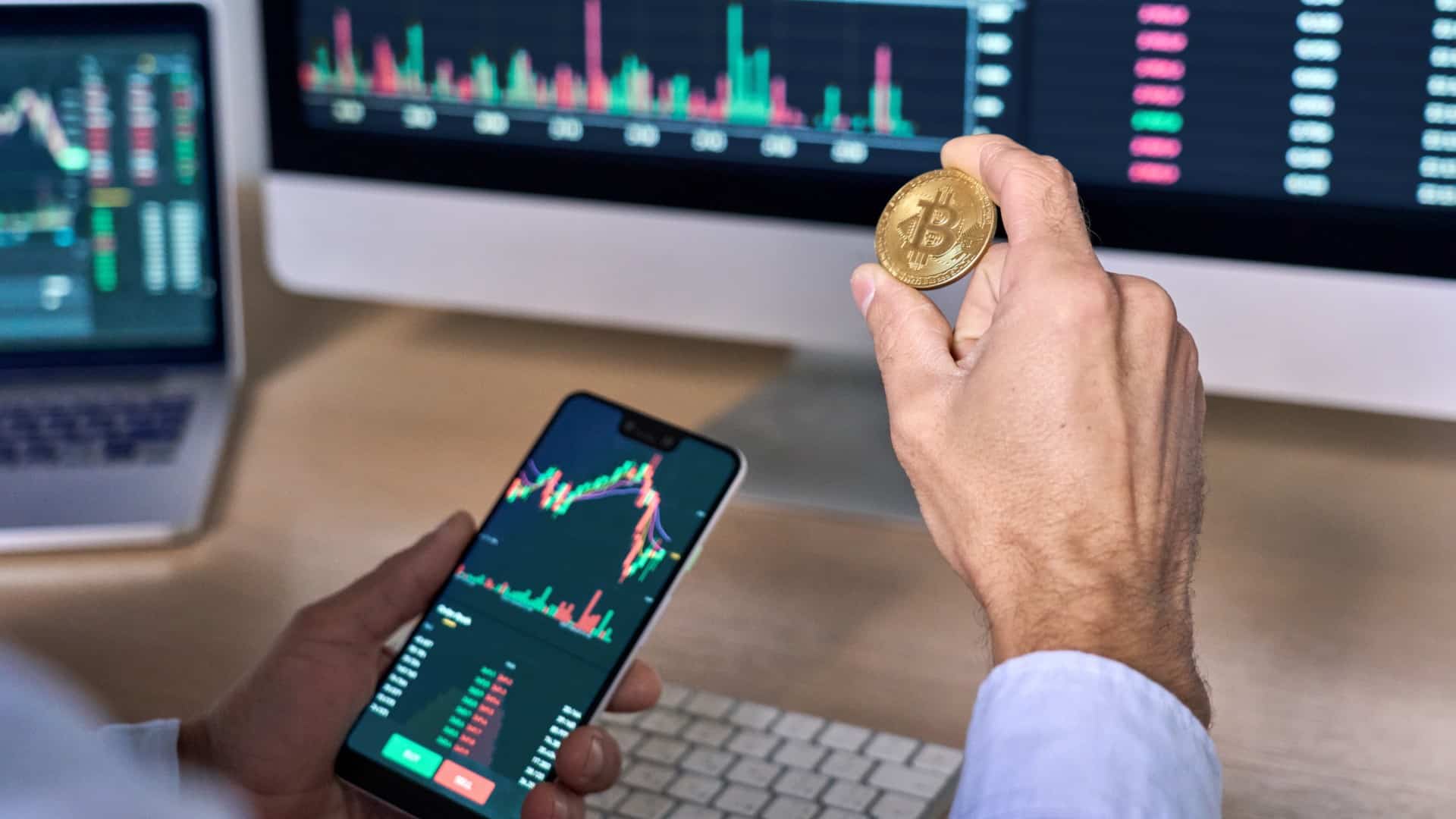 Trader segurando Bitcoin próximo de gráficos