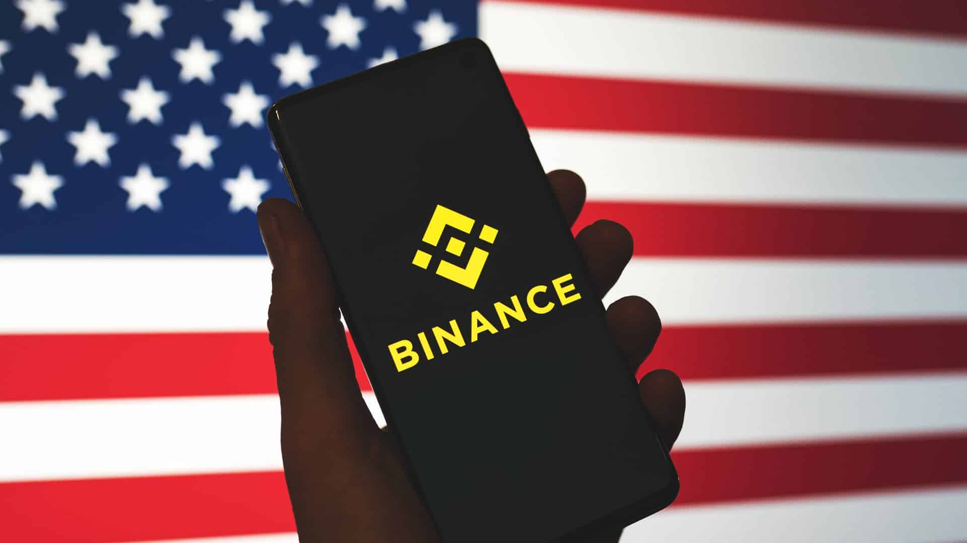 Celular com aplicativo da Binance e bandeira dos EUA.