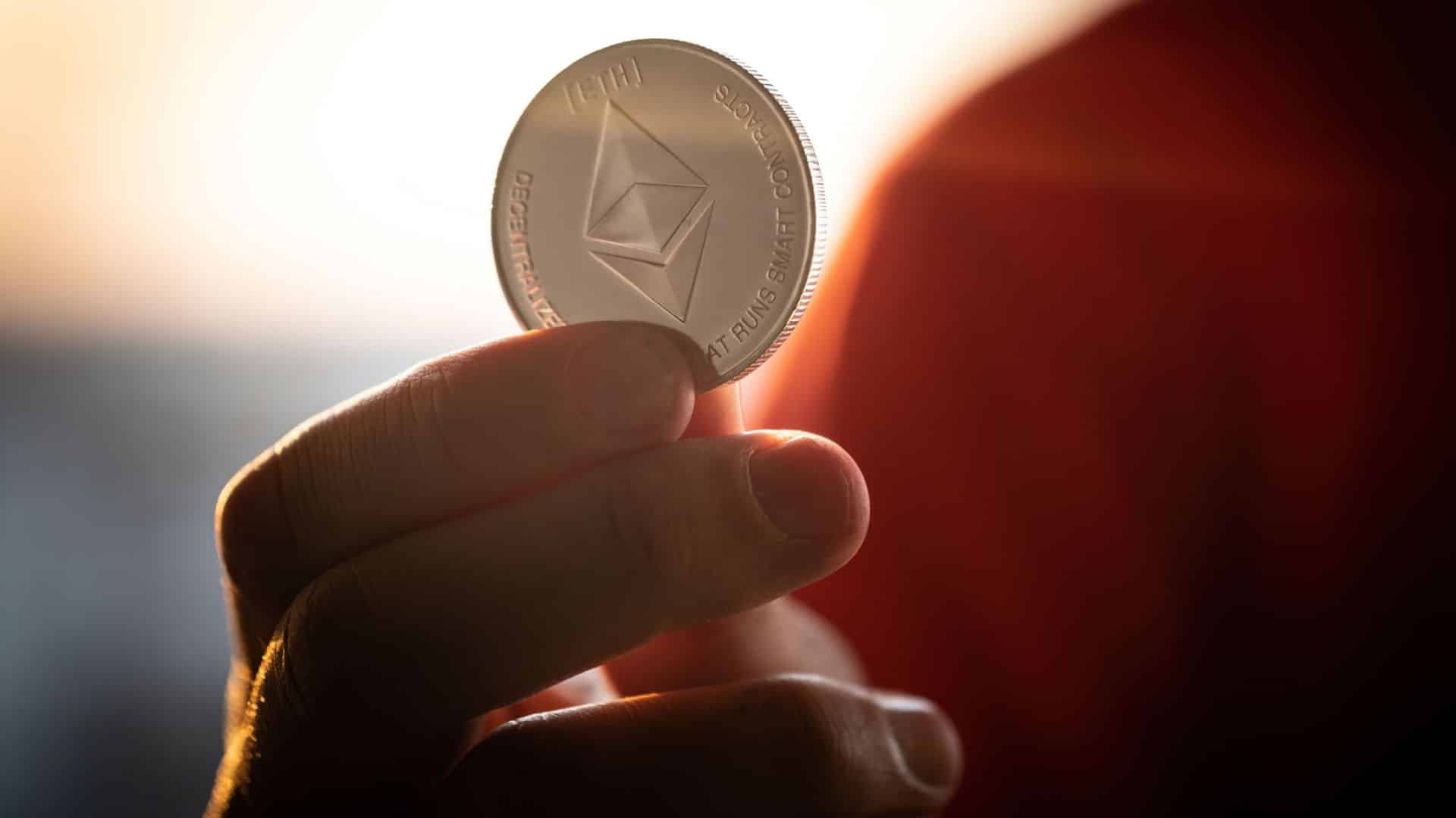 Investidor segurando moeda física de Ethereum.