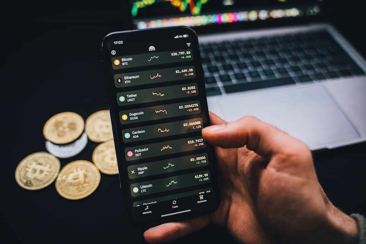 Investidor de criptomoedas observando telas de cotações com moedas simbólicas sobre a mesa próxima