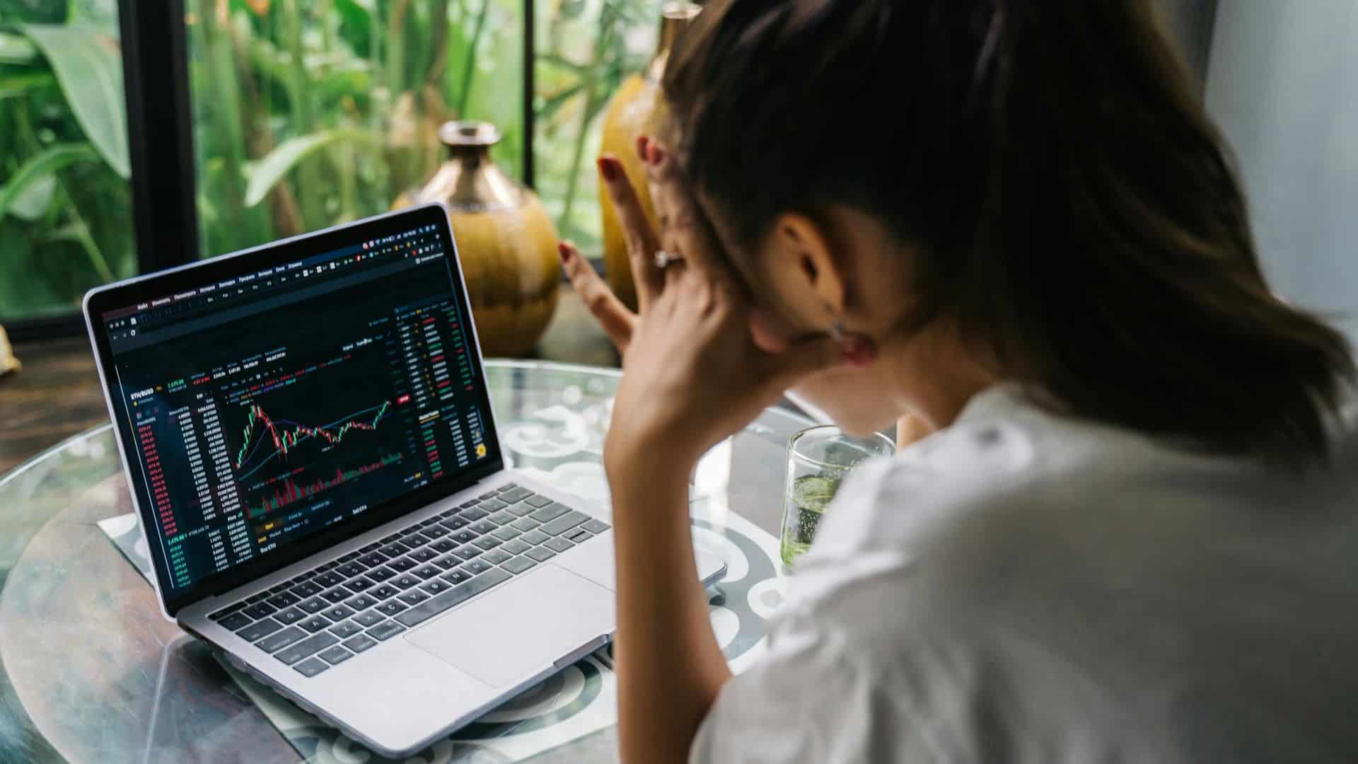 Investidora preocupada com seus investimentos olhando para tela de cotações em queda