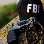Boné com escrita FBI próximo de revólver e algemas criptomoedas