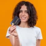 Mulher segurando cartão com fundo laranja banco do brasil brasileira criptomoedas