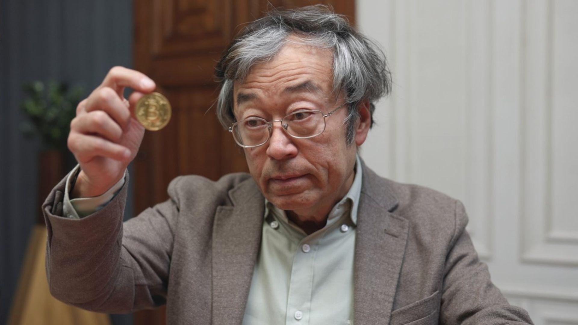 Imagem sátira de Dorian Nakamoto observando bitcoin na mão Satoshi