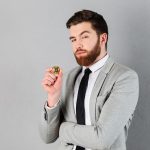 Homem com olhar desconfiado ao segurar bitcoin Coinbase Brasil