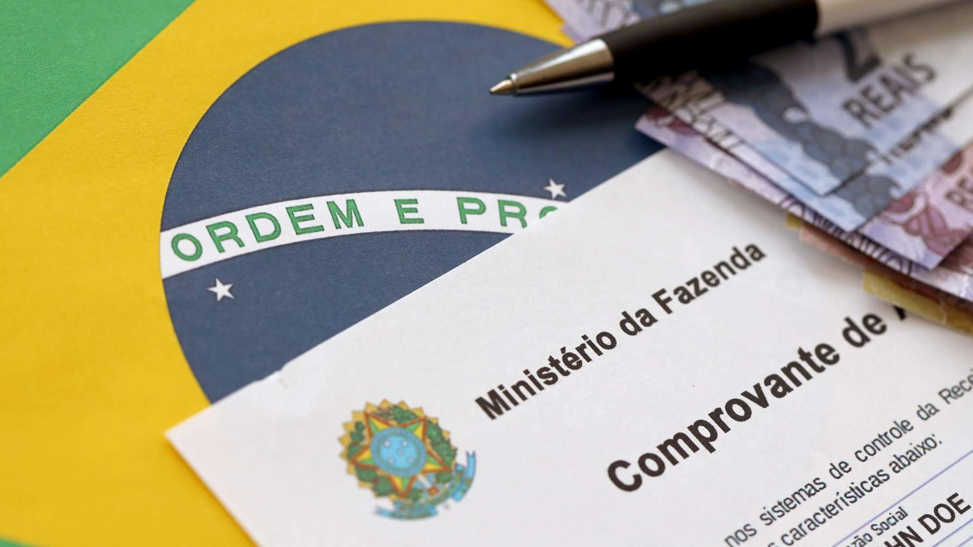 Bandeira do Brasil com papel de dinheiro e do Ministério da Fazenda próximos Receita Federal criptomoedas OCDE