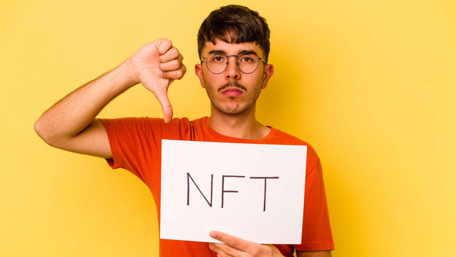 Homem com placa escrita NFT e apontando dedo para baixo em sinal pessimista Plataforma de NFTs encerra operações, culpa mercado e alerta colecionadores sobre obras