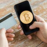 Cartão próximo de celular com símbolo do bitcoin