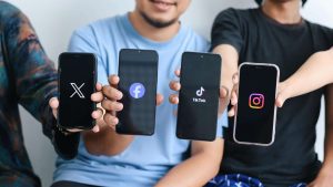 Pessoas segurando celulares com aplicativos do Facebook, Instagram, X e TikTok Twitter